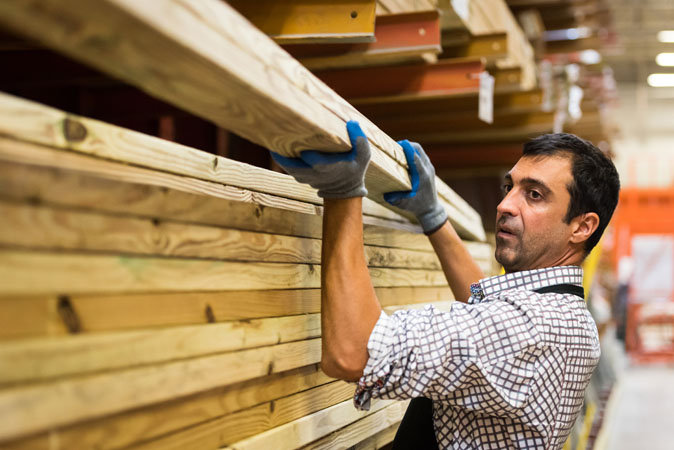 An employee stacks lumber on a shelf at a hardware store.