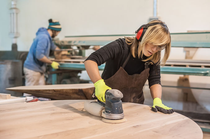 A carpenter using an electrical sander to resurface a large piece of wood.