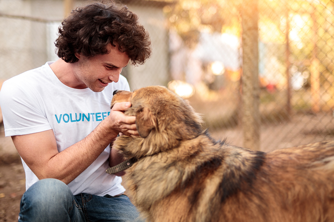 A happy pet shelter volunteer caresses a large furry dog.